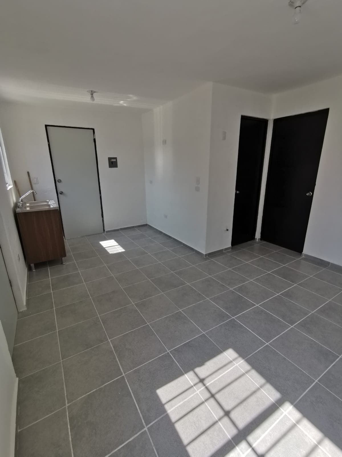 Sala amplia con piso de loseta gris y cocina compacta